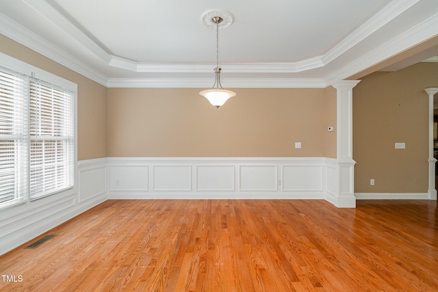 spare room with light hardwood / wood-style flooring, a raised ceiling, crown molding, and decorative columns