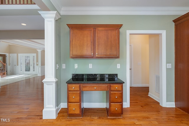 kitchen featuring dark stone countertops, decorative columns, ornamental molding, and light hardwood / wood-style flooring