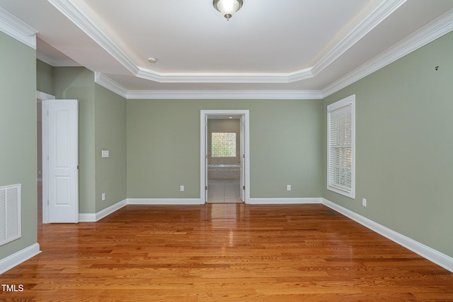 empty room featuring wood-type flooring, a raised ceiling, and crown molding