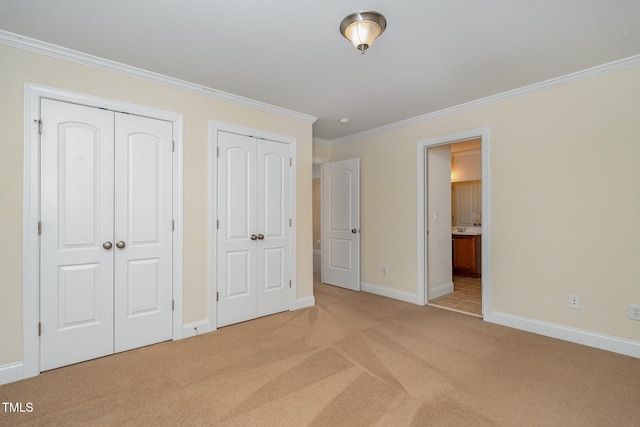 unfurnished bedroom featuring light colored carpet, ensuite bath, multiple closets, and crown molding