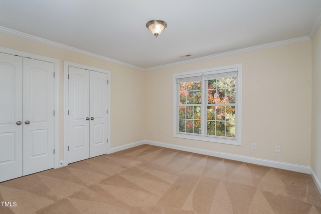 unfurnished bedroom featuring light colored carpet, two closets, and crown molding