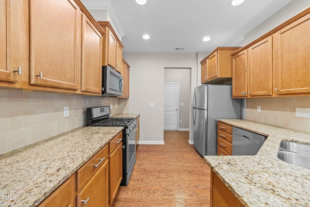 kitchen with light stone countertops, appliances with stainless steel finishes, light wood-type flooring, and decorative backsplash