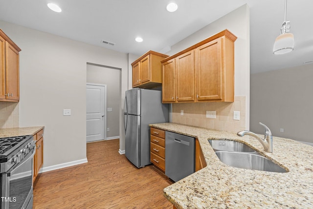 kitchen with light stone countertops, sink, stainless steel appliances, light hardwood / wood-style flooring, and decorative light fixtures