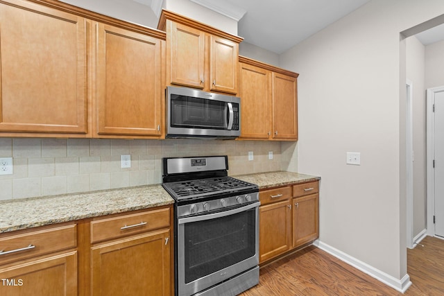 kitchen with appliances with stainless steel finishes, backsplash, light hardwood / wood-style floors, and light stone counters