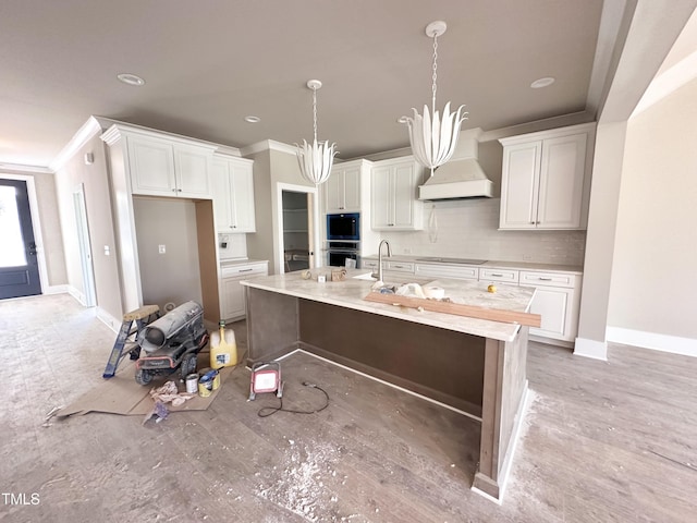 kitchen featuring custom exhaust hood, a kitchen island with sink, black appliances, white cabinets, and hanging light fixtures