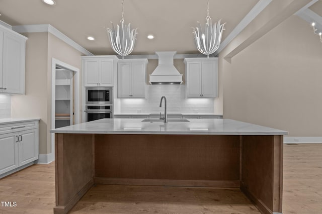 kitchen featuring light wood finished floors, premium range hood, a kitchen island with sink, and stainless steel appliances