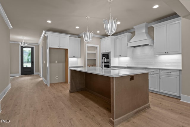 kitchen with a chandelier, a kitchen island with sink, stainless steel appliances, custom exhaust hood, and crown molding