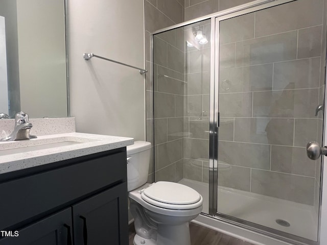 bathroom with hardwood / wood-style flooring, a shower with shower door, vanity, and toilet