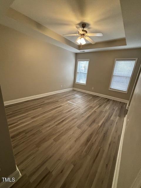 empty room with dark hardwood / wood-style flooring, a tray ceiling, and ceiling fan