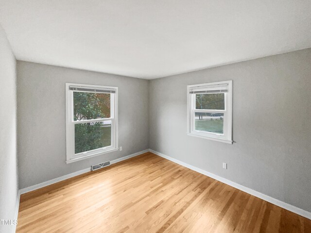 empty room featuring baseboards, visible vents, plenty of natural light, and wood finished floors