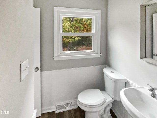 half bath featuring a sink, toilet, wood finished floors, visible vents, and baseboards