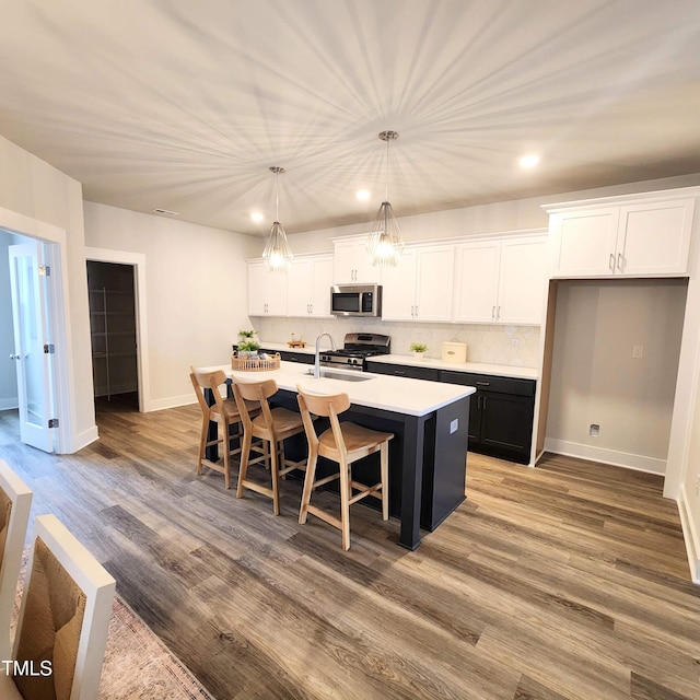 kitchen featuring hardwood / wood-style floors, an island with sink, stainless steel appliances, hanging light fixtures, and white cabinets