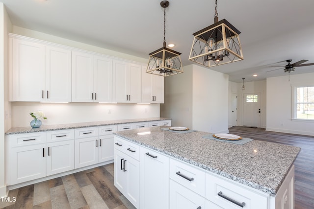 kitchen with light stone countertops, ceiling fan, a kitchen island, white cabinets, and dark wood-type flooring