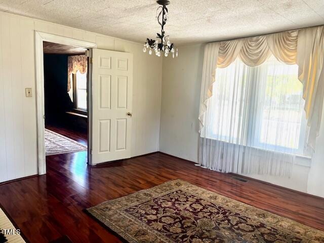 spare room featuring a textured ceiling, plenty of natural light, a chandelier, and dark hardwood / wood-style flooring