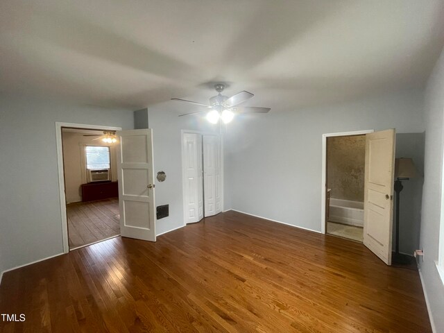 unfurnished bedroom featuring dark hardwood / wood-style flooring, cooling unit, ensuite bath, ceiling fan, and a closet