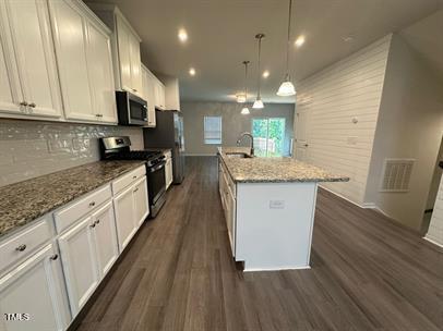 kitchen with light stone counters, white cabinetry, appliances with stainless steel finishes, decorative light fixtures, and an island with sink