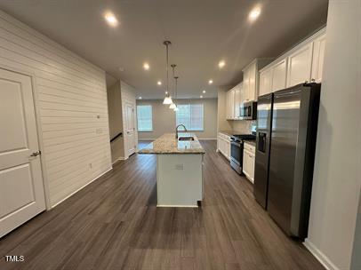 kitchen featuring dark hardwood / wood-style flooring, a center island with sink, white cabinetry, appliances with stainless steel finishes, and decorative light fixtures