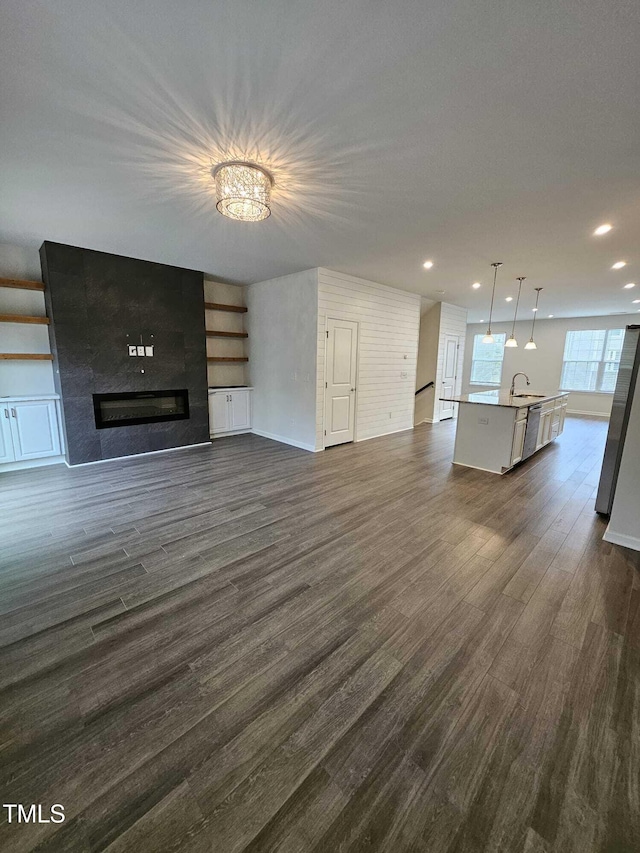 unfurnished living room featuring dark wood-type flooring, a chandelier, sink, and a large fireplace