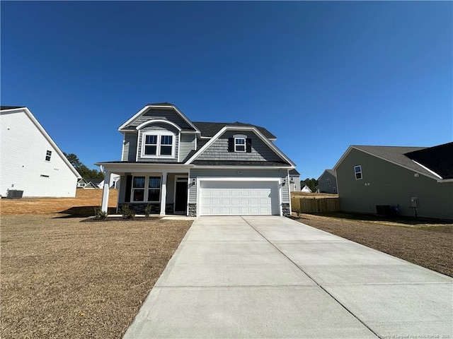 view of front of home featuring central AC unit, a garage, covered porch, stone siding, and driveway