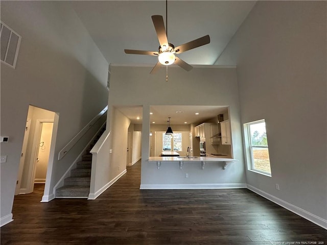 unfurnished living room featuring visible vents, dark wood finished floors, a towering ceiling, stairway, and a sink