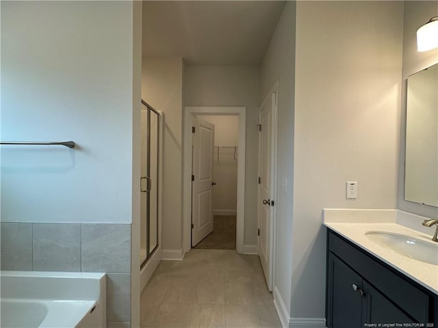 bathroom with a walk in closet, a stall shower, vanity, baseboards, and a bath