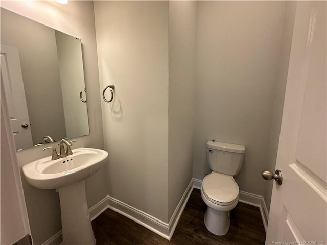 half bath featuring a sink, toilet, baseboards, and wood finished floors