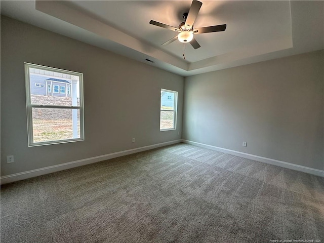 carpeted spare room with a raised ceiling, visible vents, ceiling fan, and baseboards