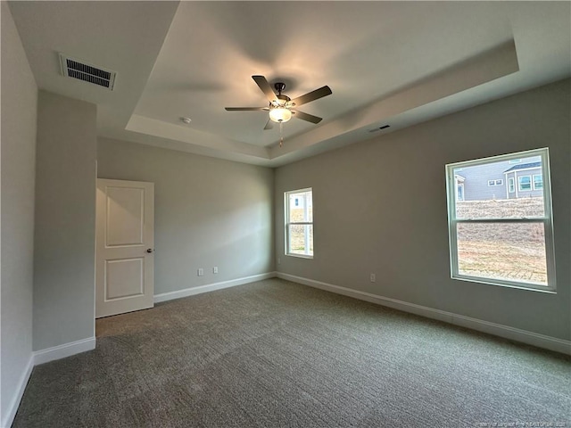 empty room with visible vents, a tray ceiling, dark carpet, and baseboards