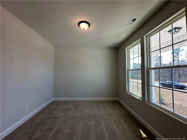 spare room featuring visible vents, dark carpet, and baseboards