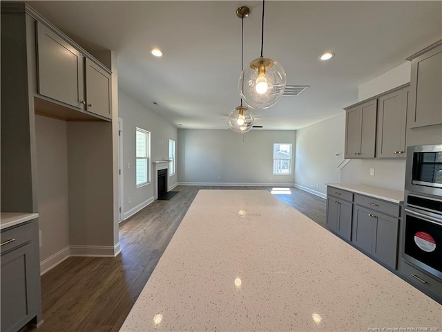 kitchen featuring appliances with stainless steel finishes, open floor plan, gray cabinetry, and light stone countertops