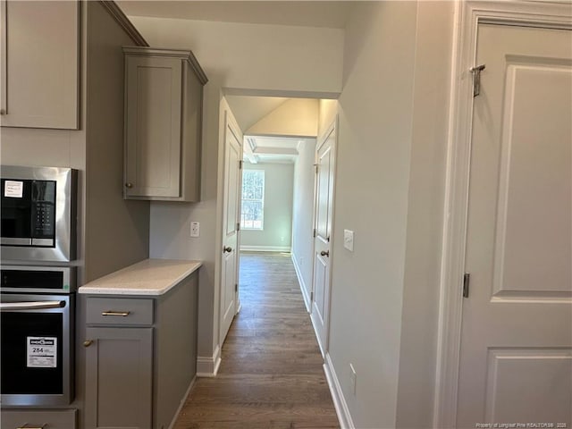 kitchen with baseboards, appliances with stainless steel finishes, wood finished floors, light countertops, and gray cabinetry