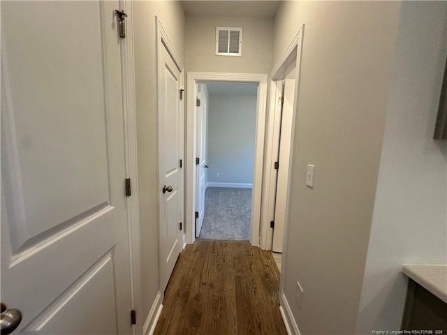 corridor featuring wood finished floors, visible vents, and baseboards