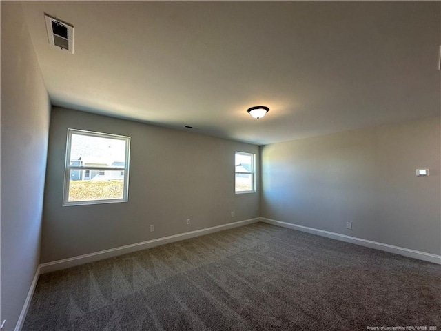 spare room with dark colored carpet, visible vents, and baseboards