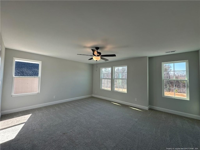 spare room featuring dark colored carpet, plenty of natural light, visible vents, and baseboards