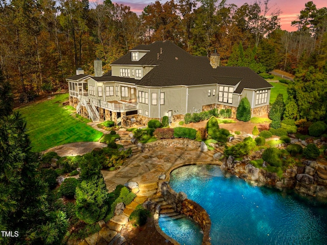 back house at dusk featuring a lawn and a swimming pool side deck