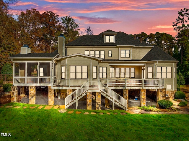 back house at dusk featuring a lawn and a sunroom