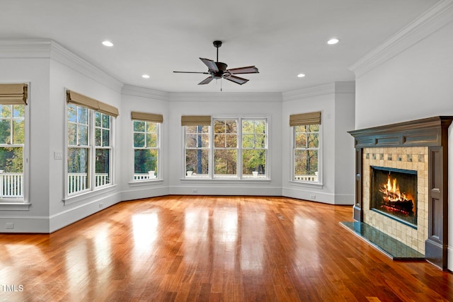 unfurnished living room with a tiled fireplace, plenty of natural light, crown molding, and light hardwood / wood-style flooring