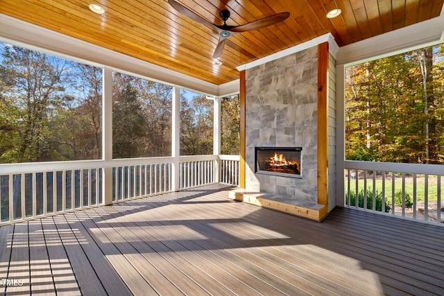 unfurnished sunroom with ceiling fan, a tile fireplace, and wood ceiling