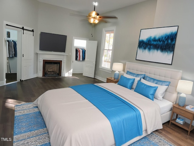 bedroom featuring dark hardwood / wood-style floors, ceiling fan, a spacious closet, a barn door, and a closet