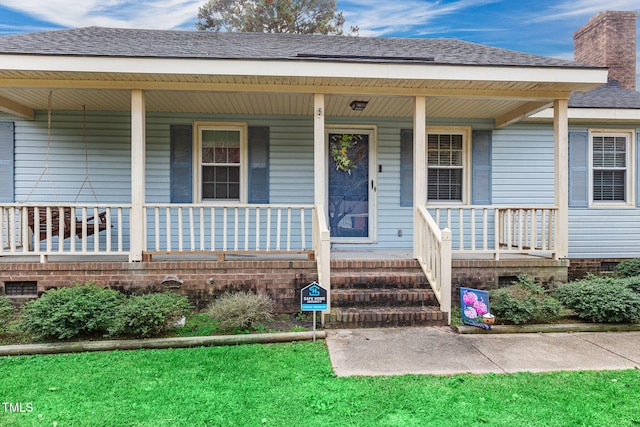 doorway to property with covered porch and a yard