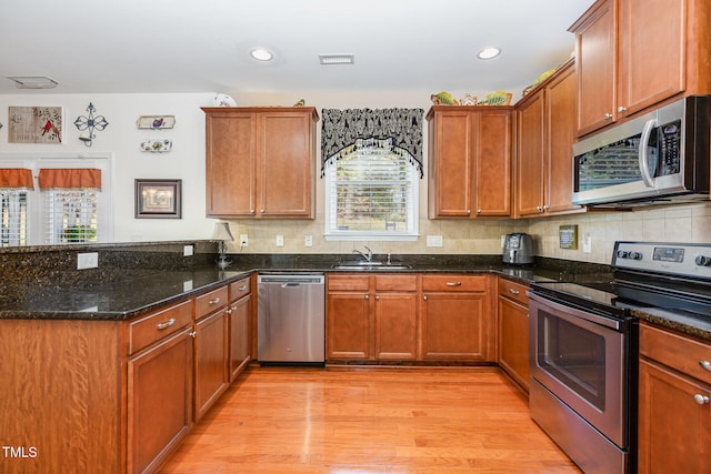 kitchen with dark stone counters, a peninsula, light wood-style floors, stainless steel appliances, and a sink