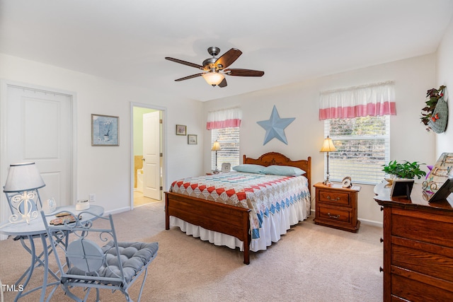 bedroom with ensuite bath, light colored carpet, baseboards, and ceiling fan