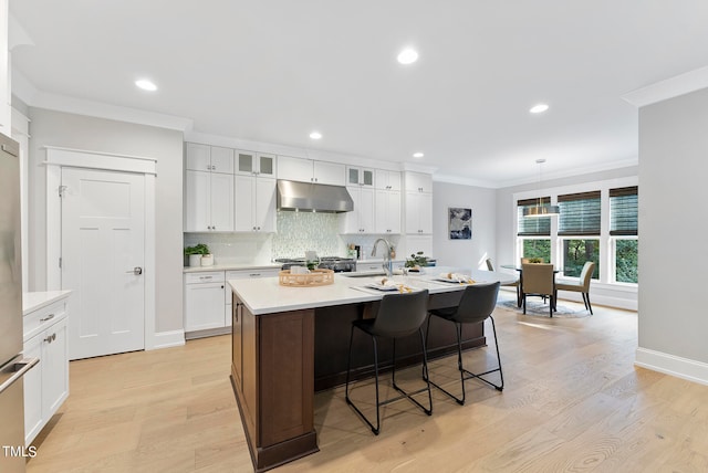 kitchen with light wood-type flooring, an island with sink, crown molding, and white cabinets