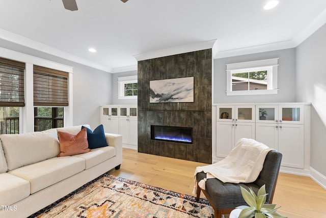 living room with ceiling fan, a tile fireplace, light wood-type flooring, and crown molding