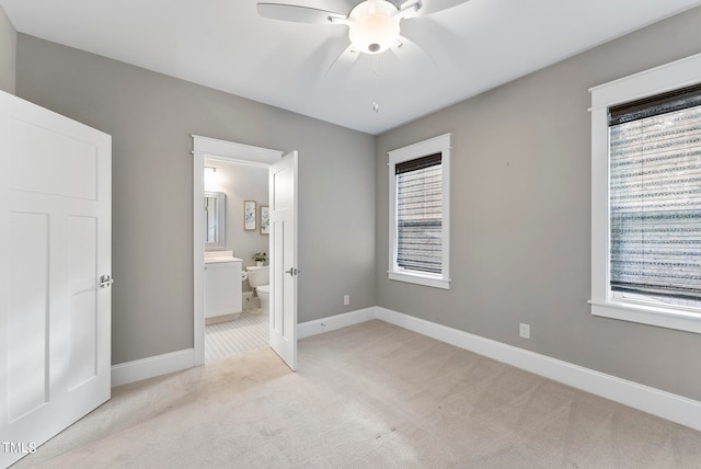 unfurnished bedroom featuring ceiling fan, multiple windows, light carpet, and connected bathroom