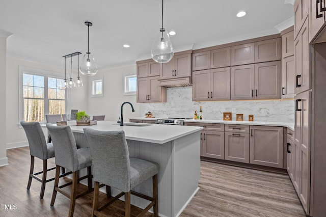 kitchen with sink, backsplash, wood-type flooring, hanging light fixtures, and an island with sink