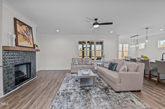 living room with ornamental molding, a tiled fireplace, ceiling fan, and wood-type flooring