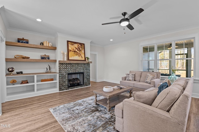 living room with light wood-type flooring, a tiled fireplace, ceiling fan, and ornamental molding