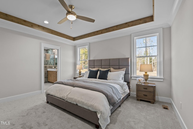 carpeted bedroom with multiple windows, ceiling fan, ensuite bathroom, and a tray ceiling