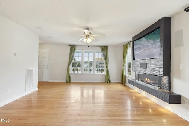 unfurnished living room with a large fireplace, ceiling fan, and light hardwood / wood-style flooring